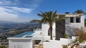 A modern villa with a rooftop infinity pool, white exterior walls, and a view of the countryside. - Villa Madi in Cumbre del Sol (Benitachell)