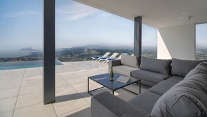 A modern living room with a large sofa, a coffee table, and a view of the ocean and cityscape. - Villa Madi in Cumbre del Sol (Benitachell)