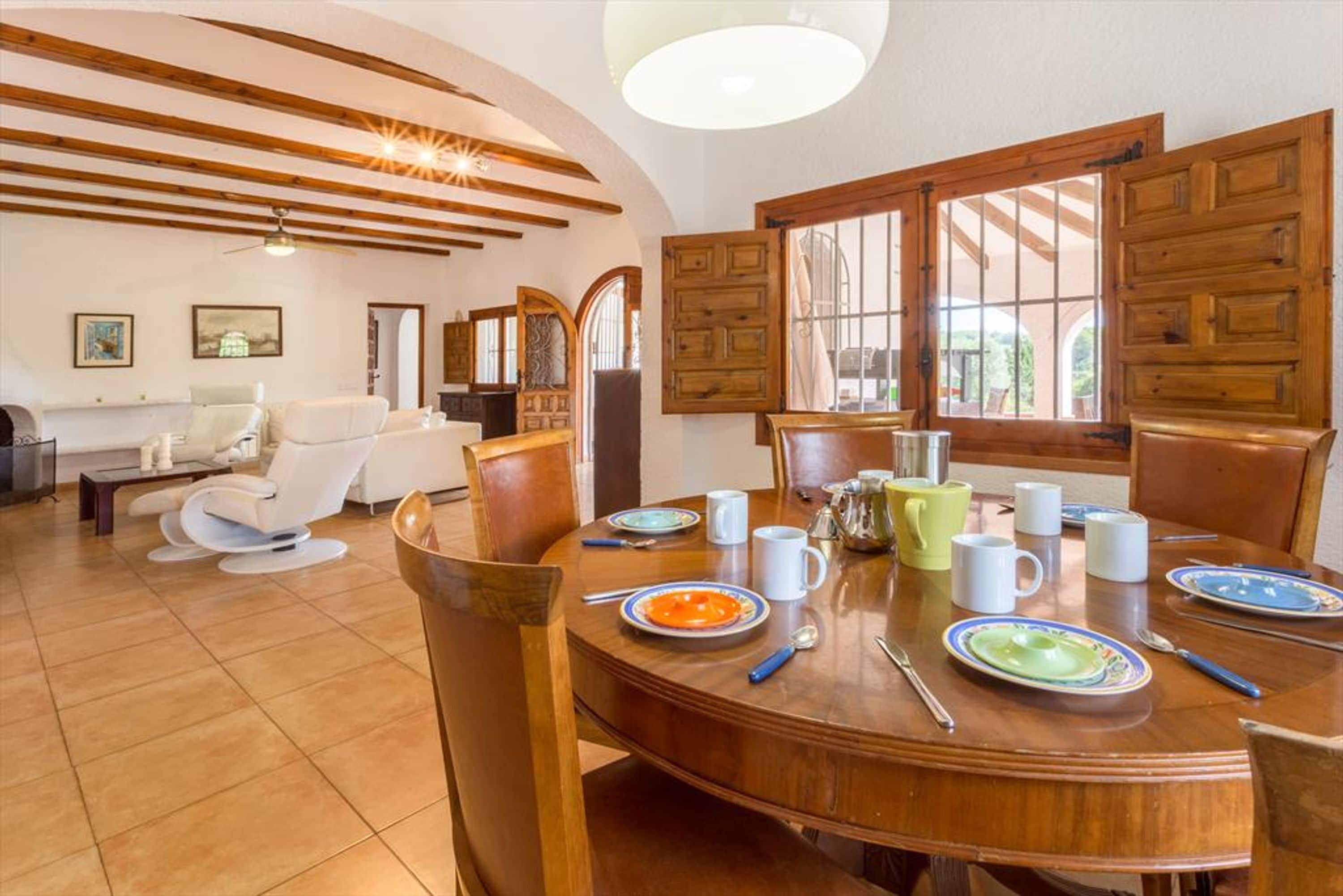Un comedor con una mesa de madera dispuesta para cuatro personas, rodeada de sillas. Hay platos, tazones y vasos sobre la mesa.