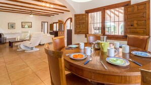 A dining area with a wooden table set for four, surrounded by chairs. There are plates, bowls, and cups on the table. - Villa Yuca in La Mandarina (Javea)