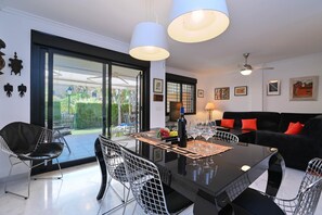 Relax in this stylish living room with a sleek dining table and comfortable sofa, surrounded by lush greenery.