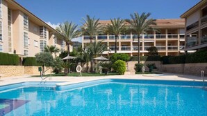 A swimming pool with a clear blue water, surrounded by palm trees and a multi-story building with balconies. - Golden in Javea With 3 Bedrooms and 2 Bathrooms (Javea)
