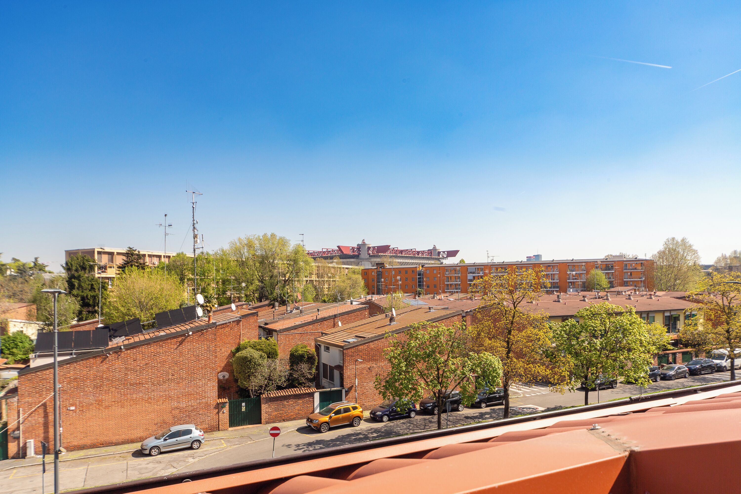A view of a street with buildings, trees, and parked cars.