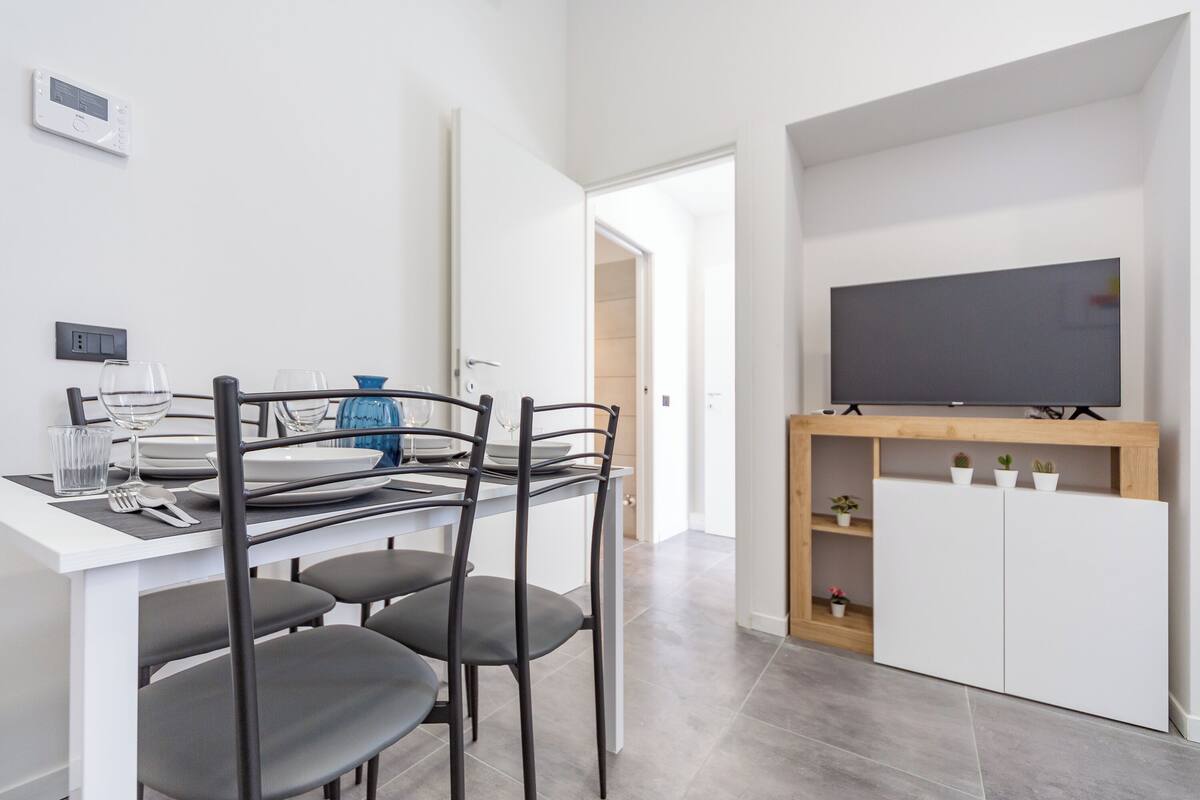 A modern kitchen with a dining area, a flat-screen TV, and a built-in cabinet with plants.