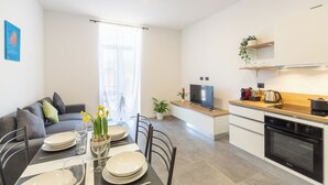 A modern kitchen with a built-in oven, a dining area with a table set for four, and a living area with a sofa and a TV. - KHL apartments (Milan)