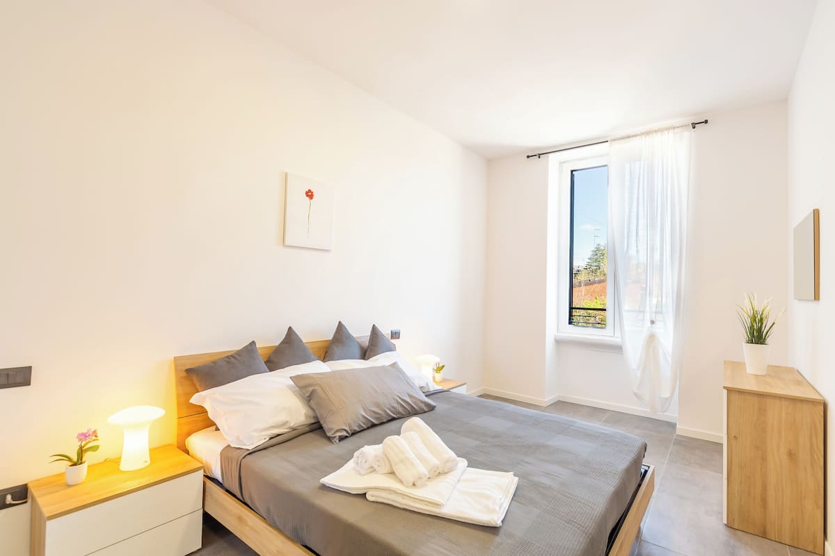 A neatly made bed with pillows, a bedside lamp, and a small plant on the nightstand.