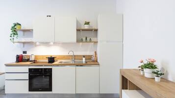 A modern kitchen with white cabinets, a wooden countertop, a built-in oven, and a sink. There are potted plants on shelves and a wooden bench.