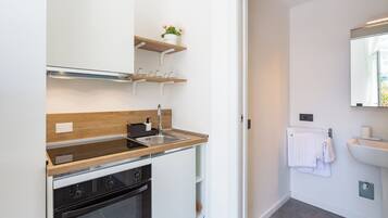 Una cocina moderna con armarios blancos, encimera de madera y horno empotrado. Hay dos repisas de madera sobre el fregadero, y una pequeña planta en maceta en la repisa superior.