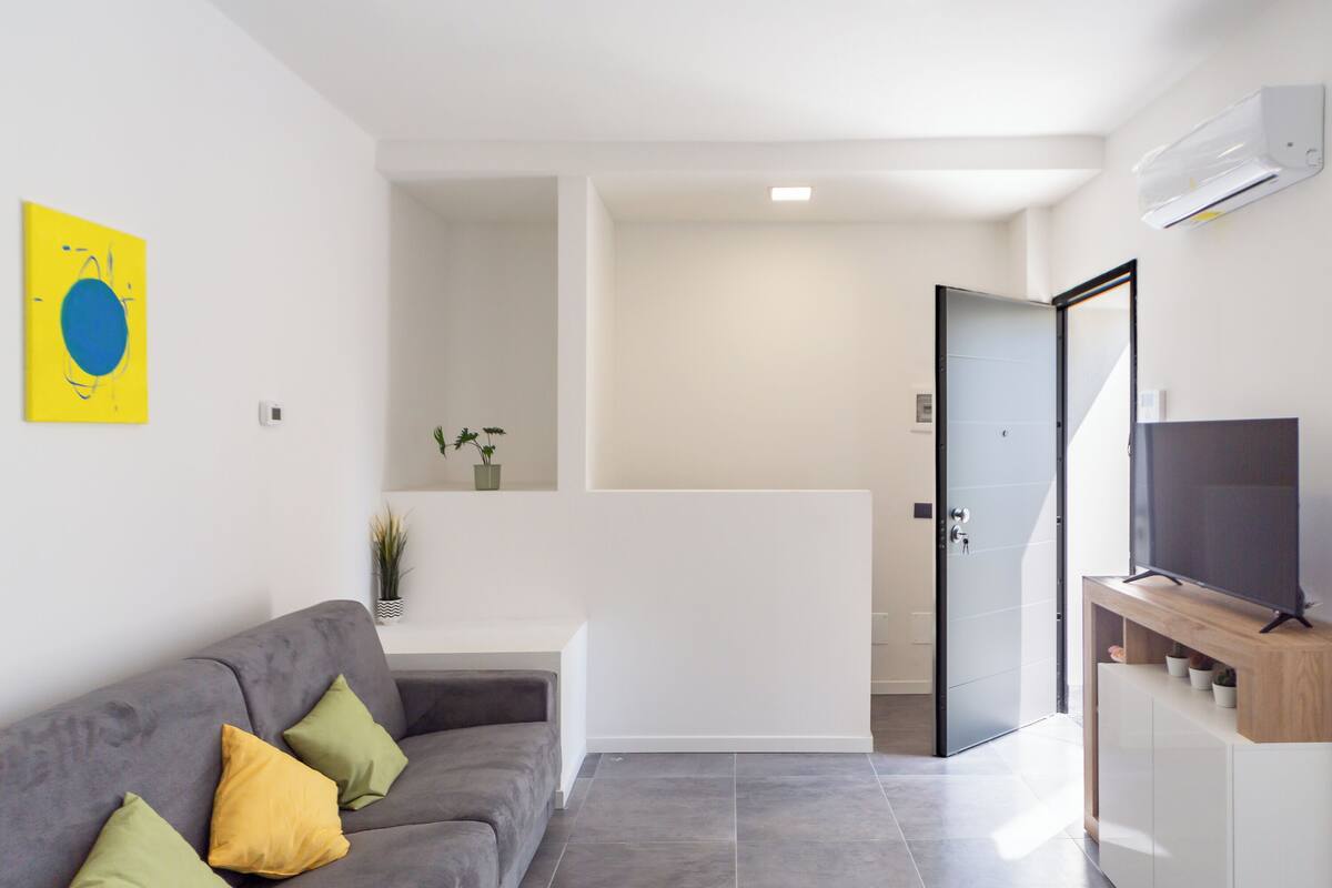A modern living room with a grey sofa, a flat-screen TV, and a minimalist design.