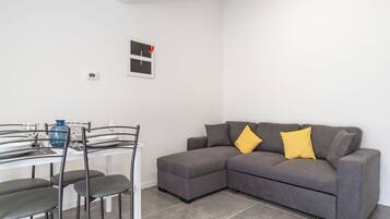 Una sala de estar moderna con un sofá seccional gris, una mesa de comedor con sillas y un jarrón azul.