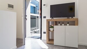 A modern living room with a TV mounted on a wooden shelf, a sliding door leading to a balcony, and a small potted plant on the shelf. - KHL apartments (Milan)