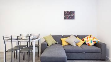 A modern living room with a grey sectional sofa, a dining table with chairs, and a small abstract painting on the wall.