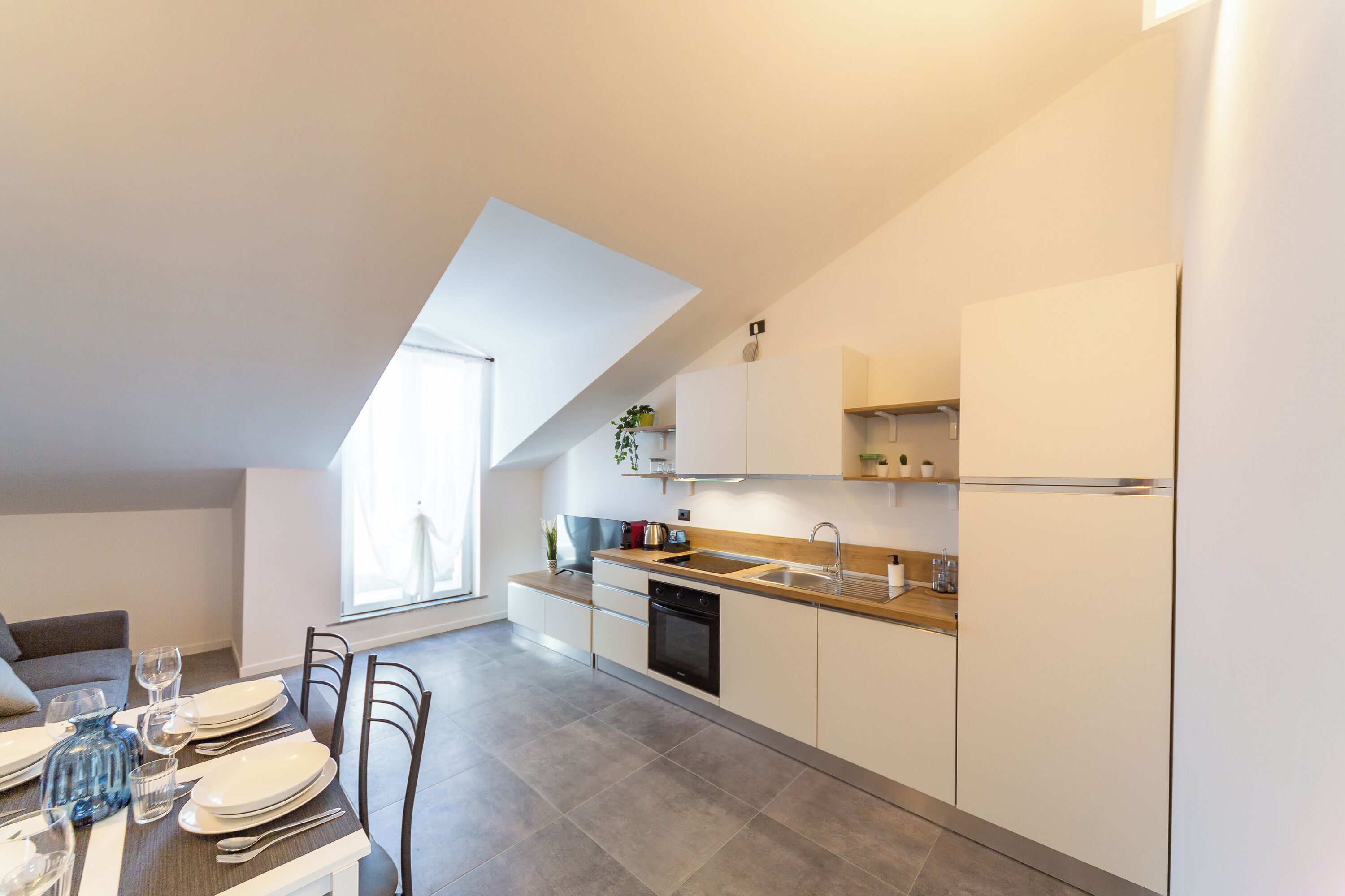 Una cucina moderna con zona pranzo, caratterizzata da un'ampia finestra, mobili bianchi e forno integrato.