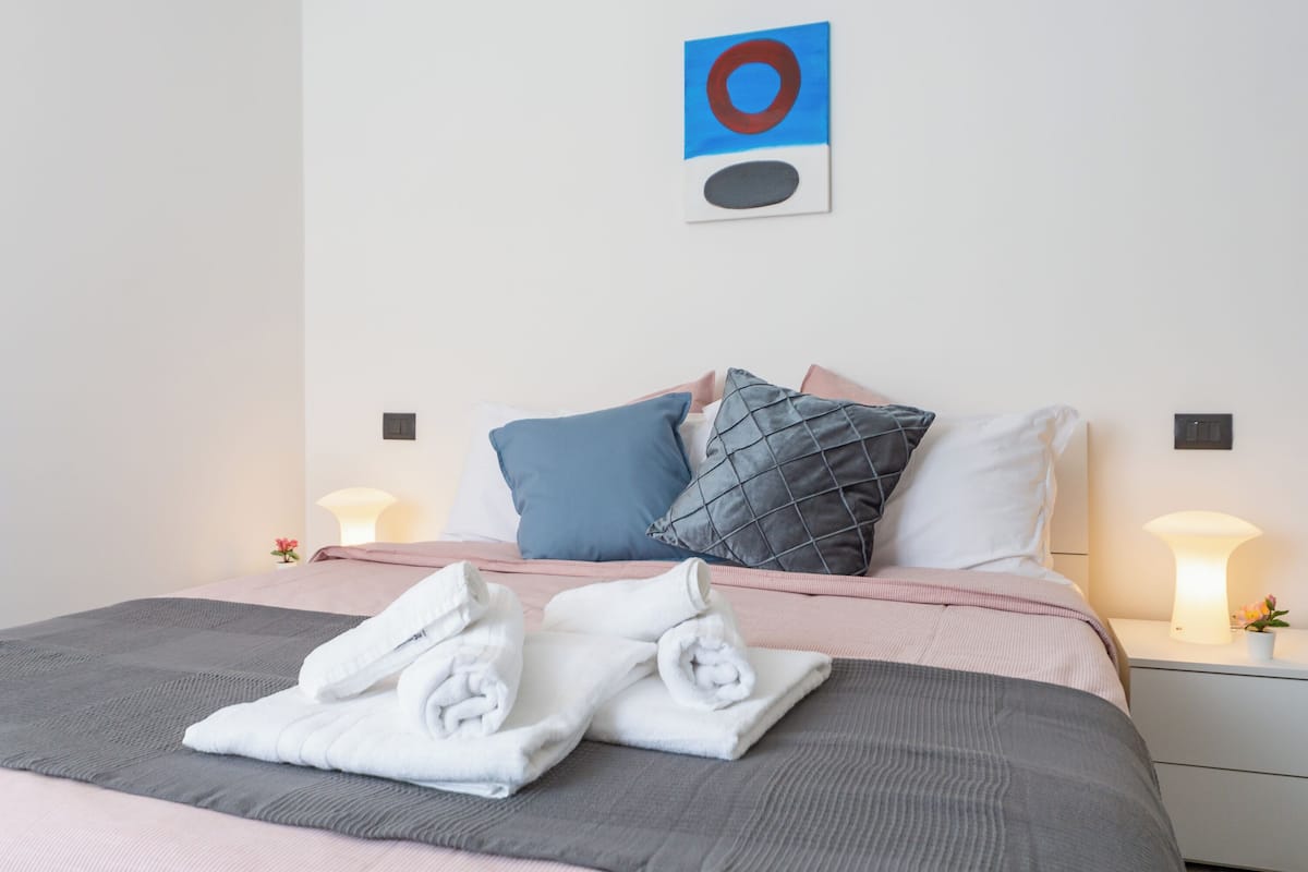 A neatly made bed with pillows, a bedside lamp, and a wall art piece.