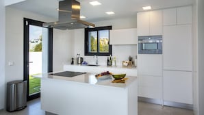 A modern kitchen with a central island, stainless steel appliances, and a view through the door. - Villa Clem in Calp With 4 Bedrooms and 3 Bathrooms (Calpe)