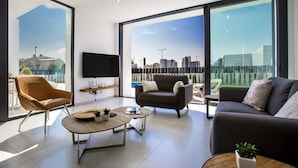 A modern living room with a sofa, armchair, and coffee table, large windows with a city view, and a flat-screen TV on the wall. - Villa Clem in Calp With 4 Bedrooms and 3 Bathrooms (Calpe)