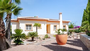 A single-story house with a tiled roof, a chimney, and a small porch. There are palm trees and a large terracotta pot in the front yard. - Villa Eva in J vea With 3 Bedrooms and 2 Bathrooms (Javea)