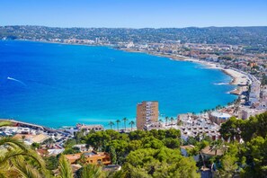 Un paysage urbain côtier avec une plage bien visible, des eaux d’un bleu limpide et un mélange de bâtiments résidentiels et commerciaux.
