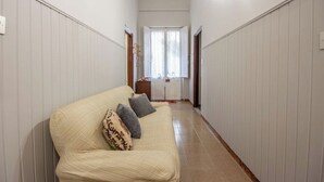 Un couloir étroit avec un canapé de couleur crème et deux coussins, bordé de murs blancs à panneaux et doté d’un plancher en bois.