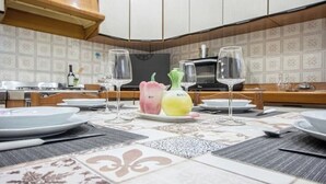 Une cuisine avec des meubles blancs, un four à micro-ondes et une table à manger mise avec des assiettes, des verres et un panier de fruits.