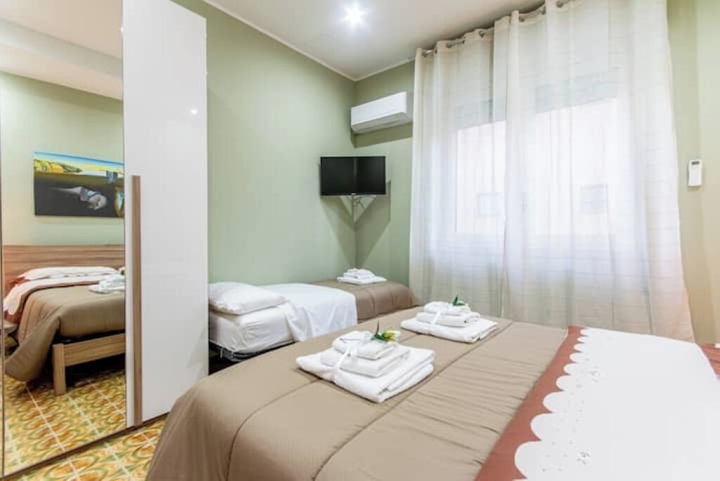 A hotel room with two beds, a flat-screen TV mounted on the wall, and a mirror reflecting the room.