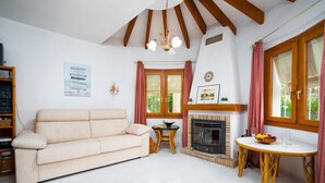 A cozy living room with a beige sofa, a fireplace, a round wooden table, and a bookshelf. - Villa Nora in El Poble Nou de Benitatxell (Benitachell)