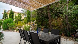 An outdoor patio with a table and chairs, surrounded by lush greenery and a stone wall. - Villa Nora in El Poble Nou de Benitatxell (Benitachell)