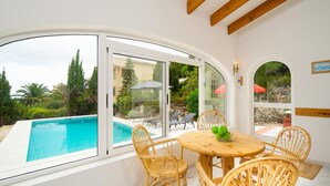 A room with a large window overlooking a swimming pool, wicker furniture, and a wooden ceiling. - Villa Nora in El Poble Nou de Benitatxell (Benitachell)