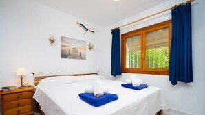 A hotel room with two beds, a nightstand with a lamp, a window with blue curtains, and a wall-mounted artwork of a bird. - Villa Nora in El Poble Nou de Benitatxell (Benitachell)
