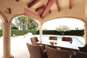 Eine Terrasse im Freien mit Pool, Korbmöbeln und Blick auf den Garten.