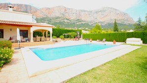 A swimming pool with a patio area, a white building with a red-tiled roof, and mountains in the background. - Fanila in J vea With 4 Bedrooms and 3 Bathrooms (Javea)