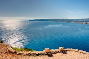 Blick auf die Küste mit einer Steinmauer im Vordergrund und einem klaren, blauen Meer bis zum Horizont.
