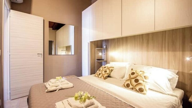 Hotellihuone, jossa on suuri sänky, vaatekaappi, peili ja yöpöytä, jossa on lamppu.