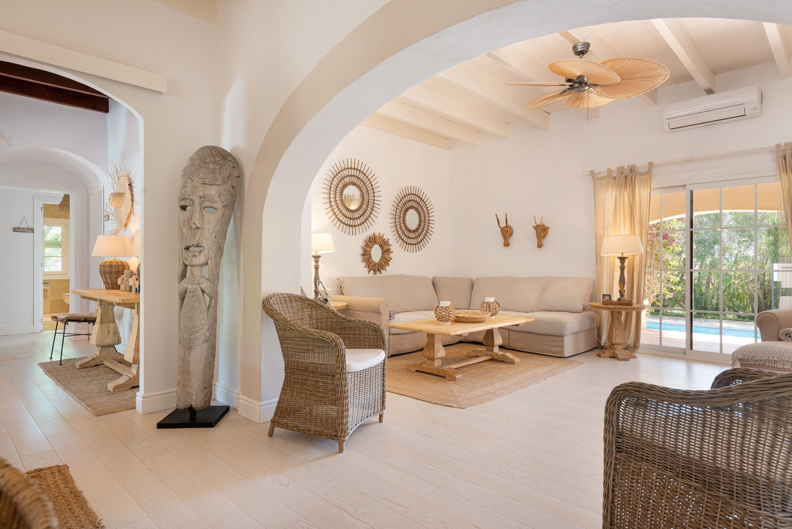 A spacious living room with a high ceiling, a large stone sculpture, wicker furniture, and decorative wall art.