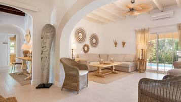 A spacious living room with a high ceiling, a large stone sculpture, wicker furniture, and decorative wall art.