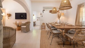 Een ruime eethoek met een lange houten tafel, rieten stoelen en een grote geweven hanglamp.