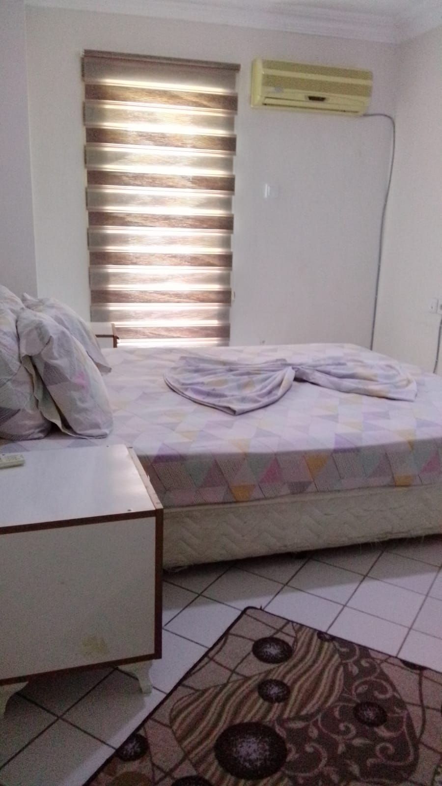 Un dormitorio con una cama, un escritorio, una ventana con persianas y un aire acondicionado de pared.