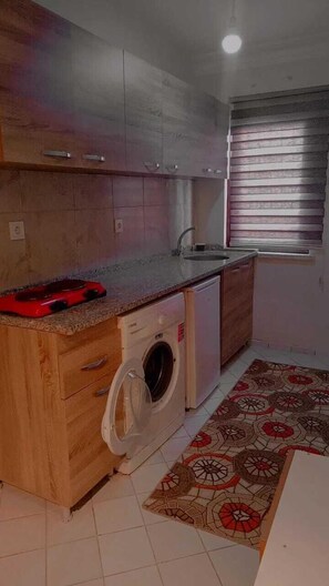 A compact kitchen with wooden cabinets, a built-in washing machine, and a small sink. - Karya Konaklama (Antalya)