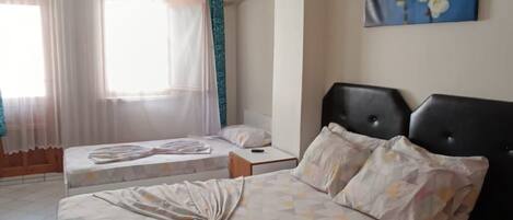 A hotel room with two beds, a ceiling fan, a painting, and a window with curtains.
