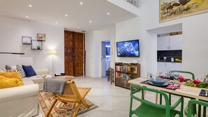 A modern living room with a sofa, a dining table set for two, a bookshelf, and a flat-screen TV mounted on the wall. - Two Levels Apt In Historical Building (Menton)