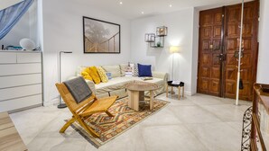 A modern living room with a sofa, a patterned rug, a wicker chair, a round coffee table, and a large wooden door. - Two Levels Apt In Historical Building (Menton)
