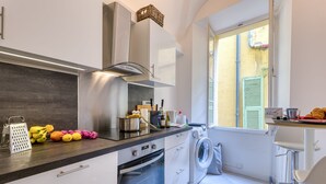 A modern kitchen with a built-in oven, a washing machine, and a window with shutters. - Two Levels Apt In Historical Building (Menton)