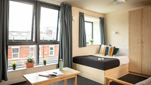 Un dormitorio pequeño con cama, una mesita, una ventana con cortinas y vistas al exterior.