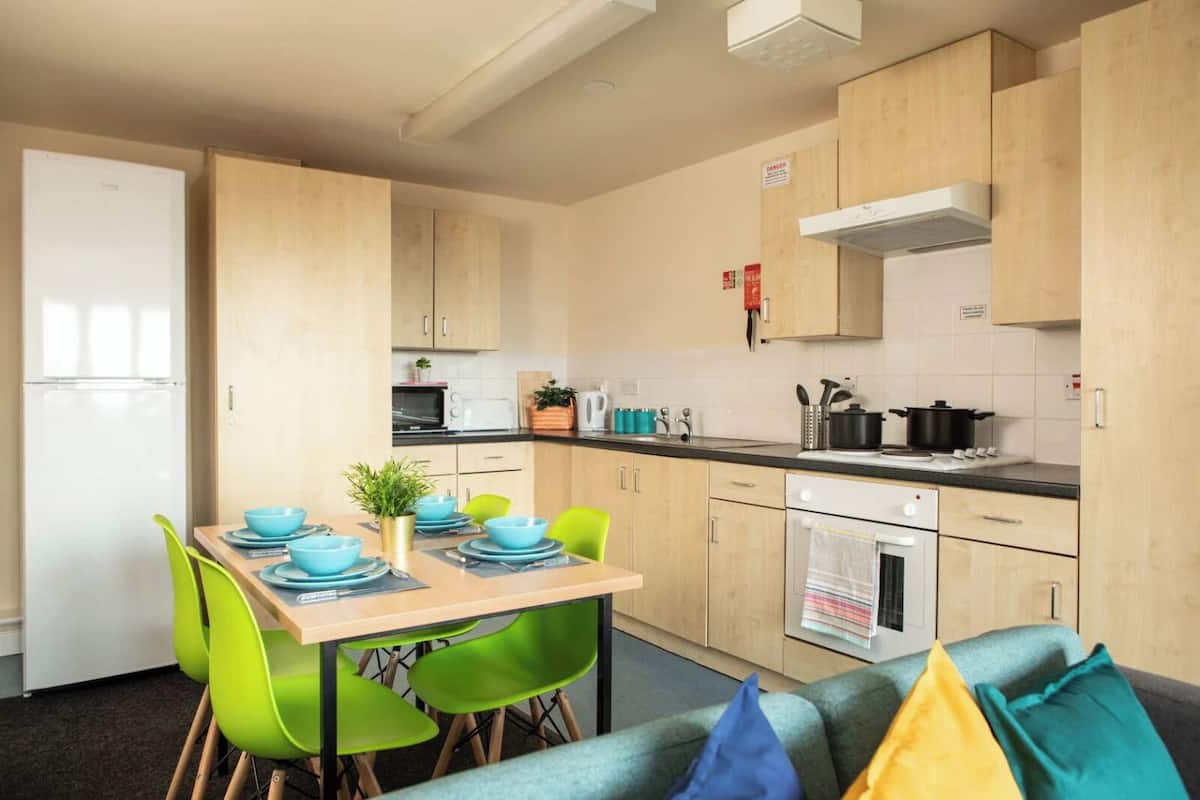 Une cuisine compacte avec un coin repas, comprenant une table dressée avec des bols et des assiettes bleus, des chaises vertes et un canapé avec des coussins.