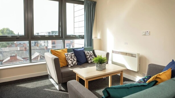 Una sala moderna con un sofá, una mesa de centro y un radiador. Amplias ventanas ofrecen vistas de la ciudad.