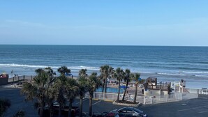 A beach view with palm trees, a parking lot, and a boardwalk leading to the beach. - Coastal Tides Ocean View Studio (Daytona Beach)