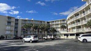 A multi-story hotel with balconies, parked cars, and palm trees. - Coastal Tides Ocean View Studio (Daytona Beach)