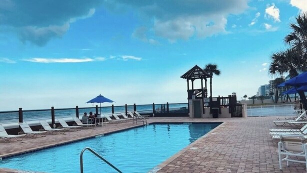A pool area with lounge chairs and a gazebo overlooking the ocean. - Coastal Tides Ocean View Studio (Daytona Beach)