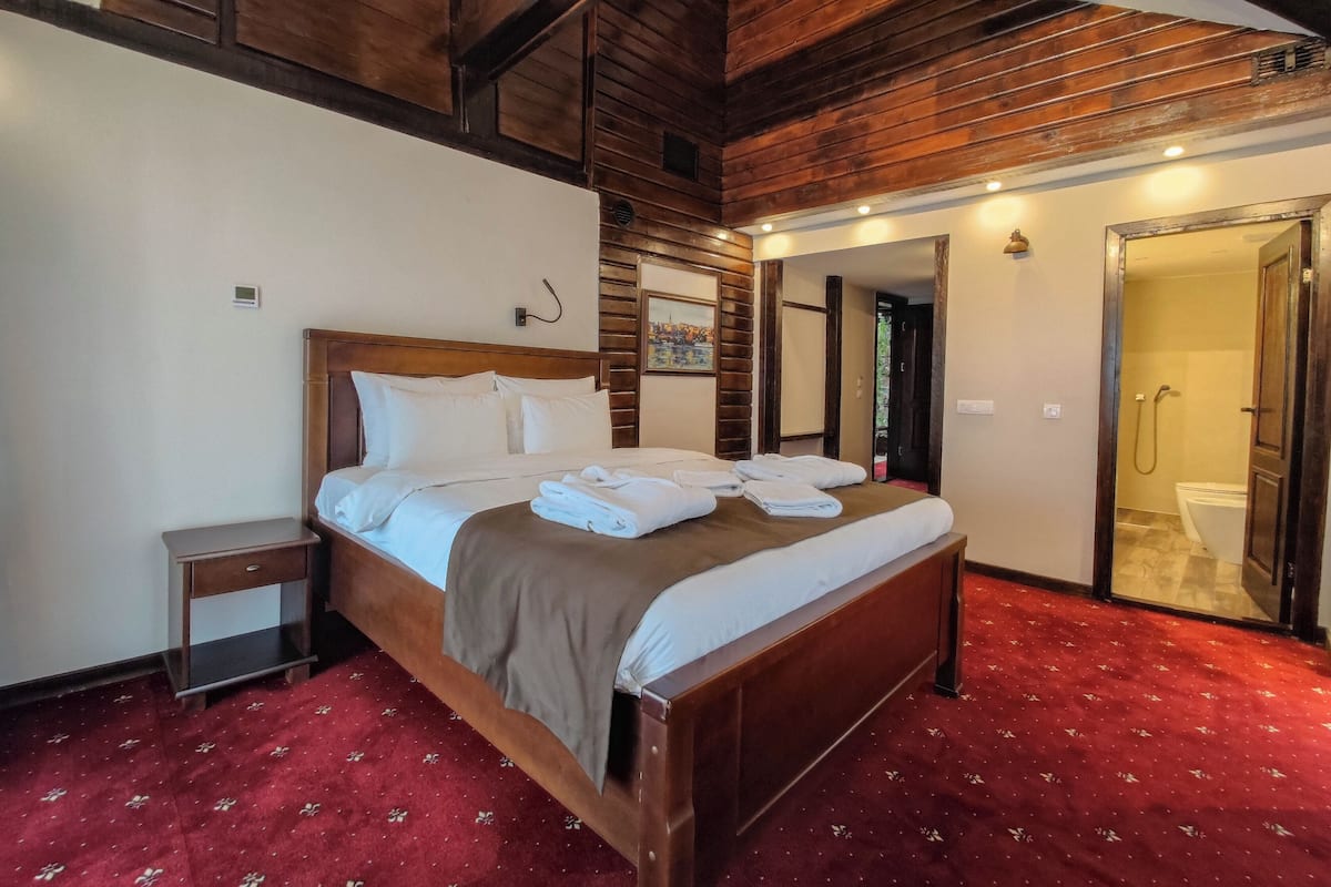 Una habitación de hotel con una cama de madera, una alfombra roja y un techo de madera.