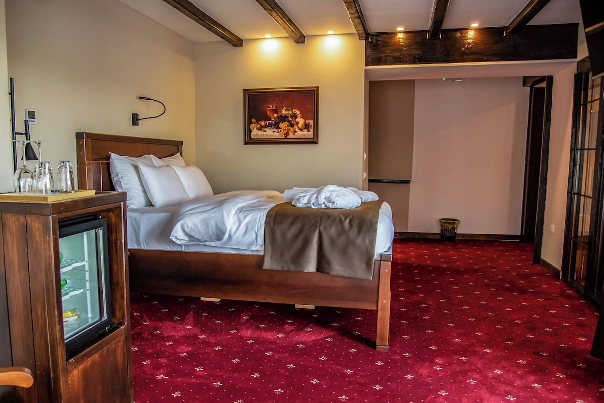 Una habitación de hotel con una cama de madera, alfombra roja, un cuadro en la pared y una pequeña mesa con vasos.